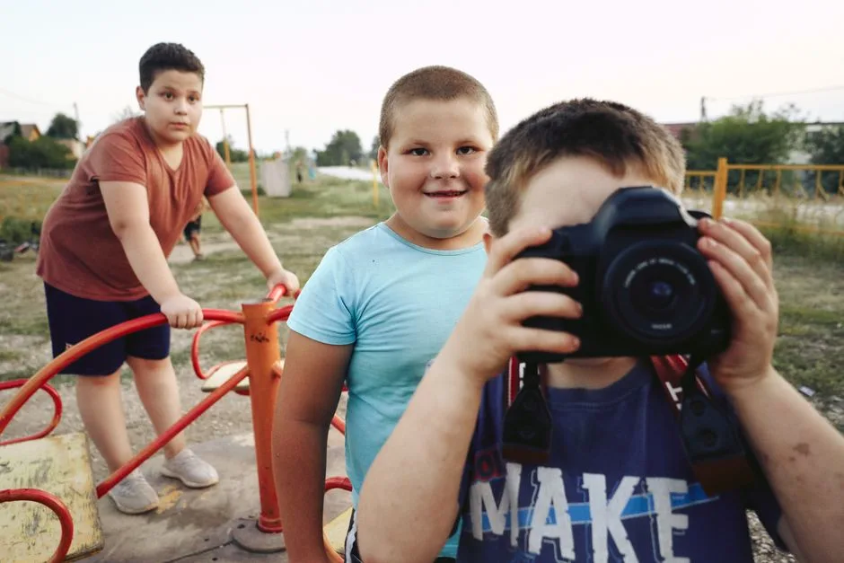 Three boys having fun with a camera at an outdoor playground, capturing moments and smiles.