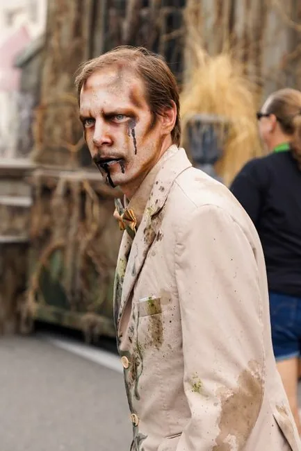 A convincing zombie in a white suit with artistic makeup outdoors during day.