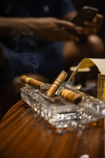 Elegant close-up of cigars in crystal ashtray with smoke curling upwards indoors.