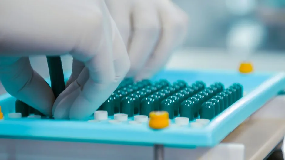 Close-up of gloved hands working with capsules in a pharmaceutical lab setting.