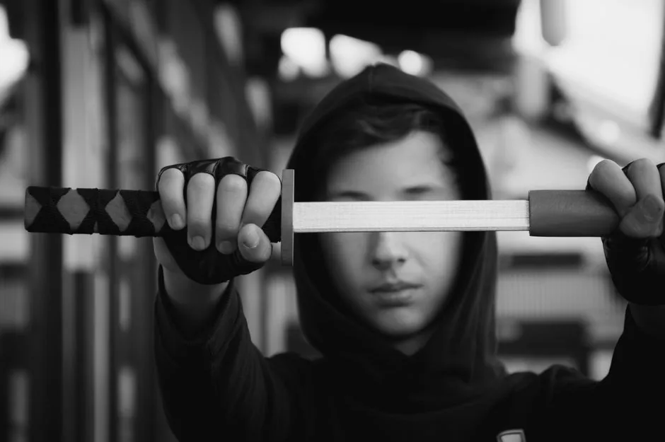 Black and white image of a teenager holding a katana, focused expression.