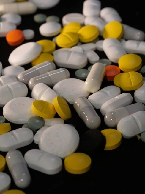 A diverse collection of pills and capsules in various colors on a dark background, emphasizing health and medicine.