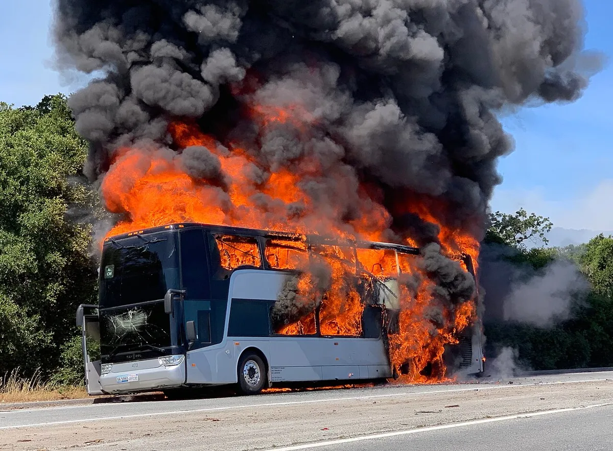 A bus engulfed in flames on the shoulder of a highway