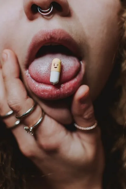 Artistic close-up of a pill on a woman's tongue with a piercing and rings.