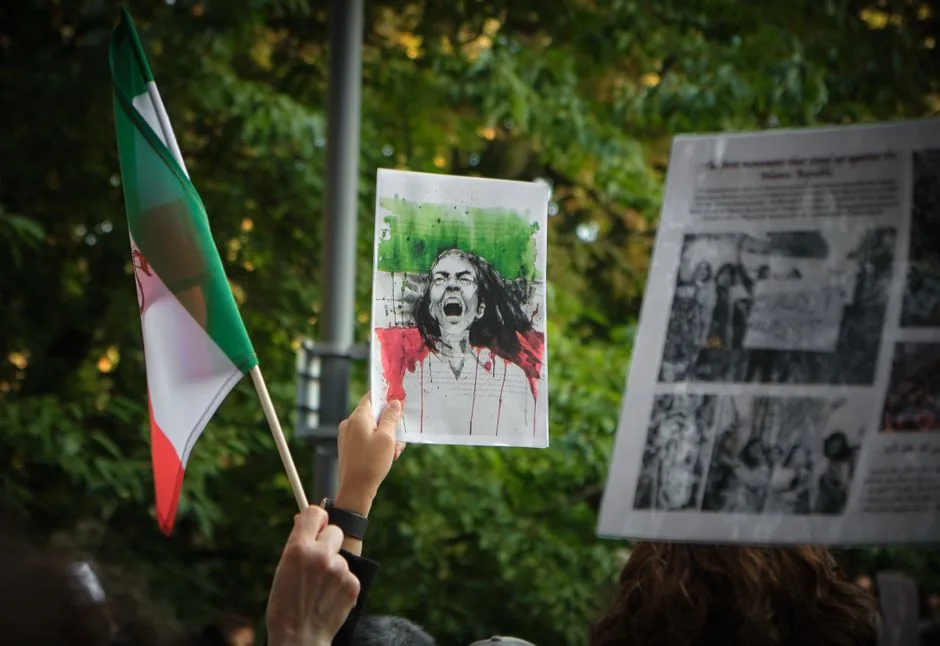 Protesters in Stockholm hold signs and an Iranian flag during a demonstration for social change.