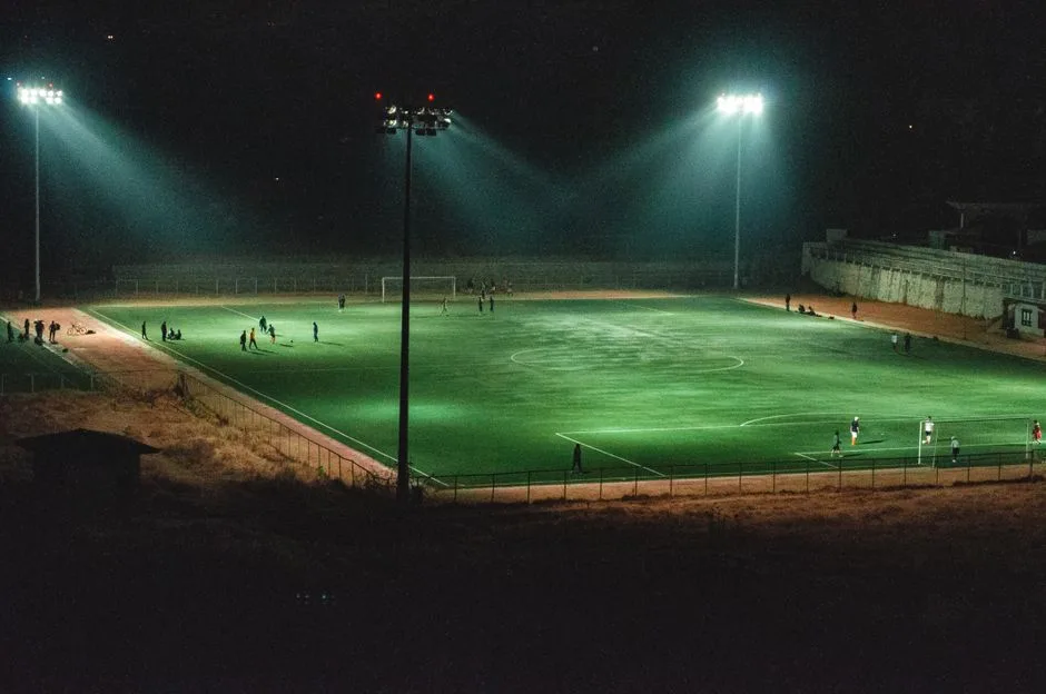 A vibrant nighttime soccer match in an illuminated stadium in Paro, Bhutan, captured from an elevated angle.