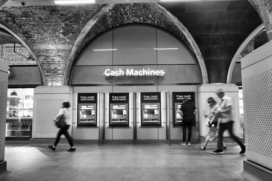 Black and white photo of people using cash machines in a metro station.