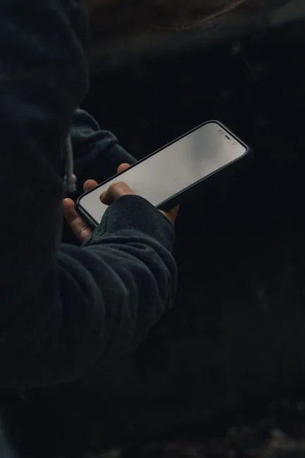 Crop anonymous person in casual clothes standing and using smartphone against dark background