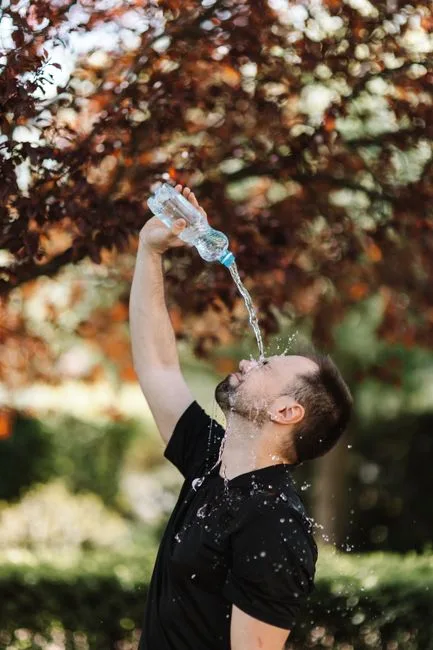 Man in black shirt pouring water from a bottle outdoors, refreshing scene.