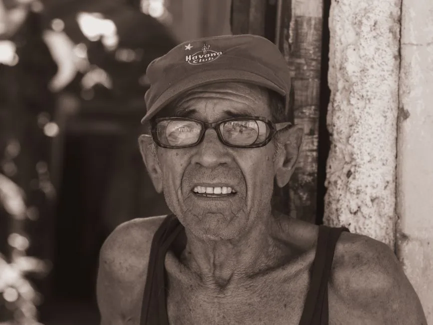 Portrait of an elderly man wearing a cap and glasses, in sepia tones.