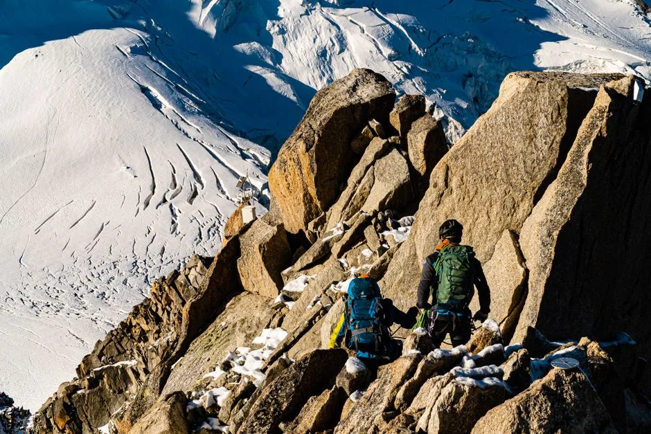 Two climbers make their way up a rugged, snowy mountain landscape during daytime.