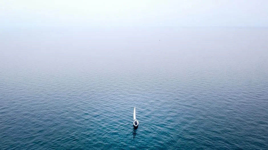 A lone sailboat sails on the serene waters of Lake Michigan under a clear sky.