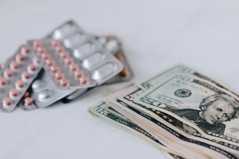 Heap of similar American dollars in cash placed near blisters of expensive drugs on white table