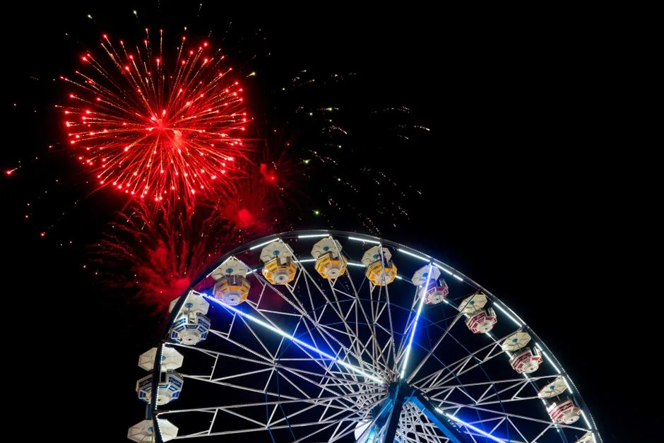 Illuminated ferris wheel and vibrant fireworks brighten Mérida, Mexico's night sky.
