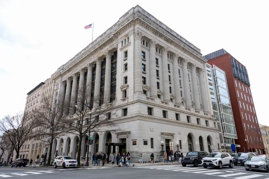 Street view of an iconic historic building in Washington D.C. with cars and pedestrians on a sunny day.