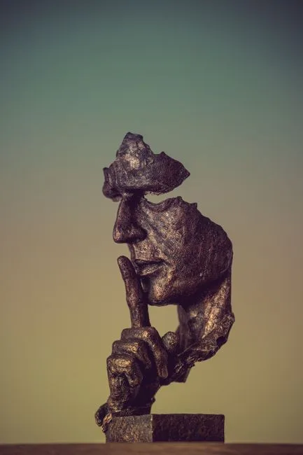 Bronze sculpture of a face missing parts and a finger to its lips, suggesting silence and mystery.