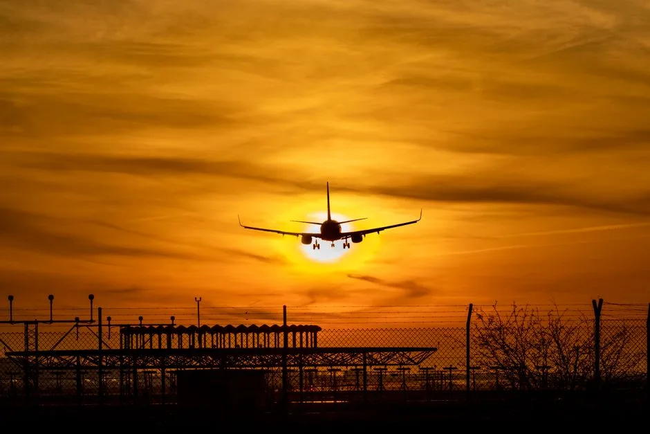 Silhouette of an airplane landing as the sun sets at El Prat Airport, highlighting vibrant orange skies.