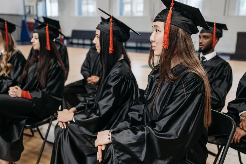 Graduates in caps and gowns seated indoors during a ceremony, celebrating academic success together.