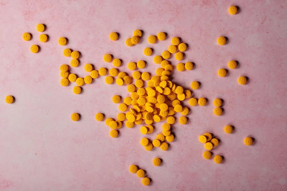 Bright yellow pills spread on a soft pink background, ideal for health and wellness themes.