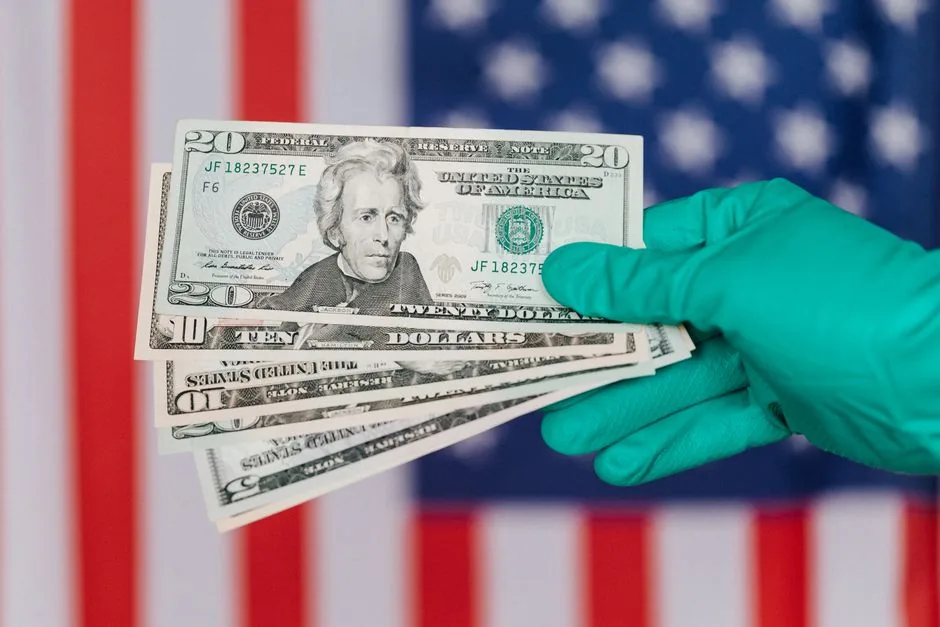Closeup anonymous person in disposable gloves showing dollars near red and blue flag of United States