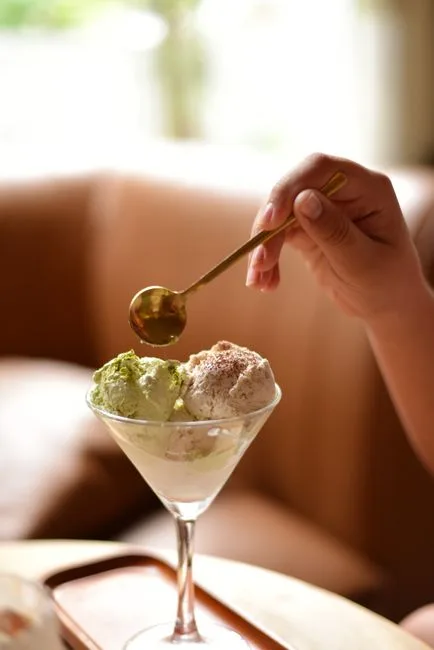 Hand holding spoon over ice cream in elegant glass bowl, indoor setting.