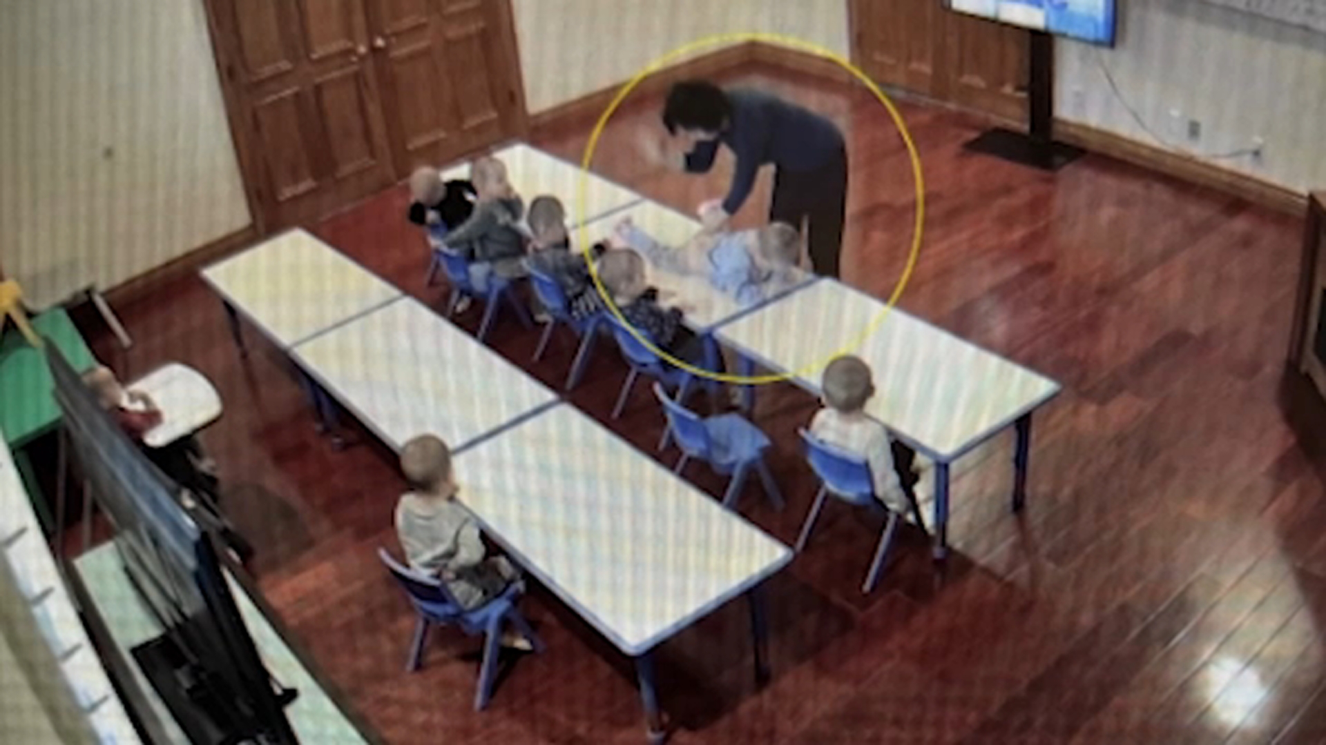Child getting spanked by nanny in front of a group of children in two rows of desks